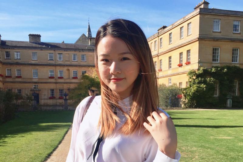Juliana Lee smiles while standing in a grassy quad between old buildings.