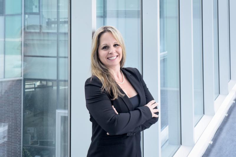 Julie McCarthy smiles, standing in a glass-walled walkway.