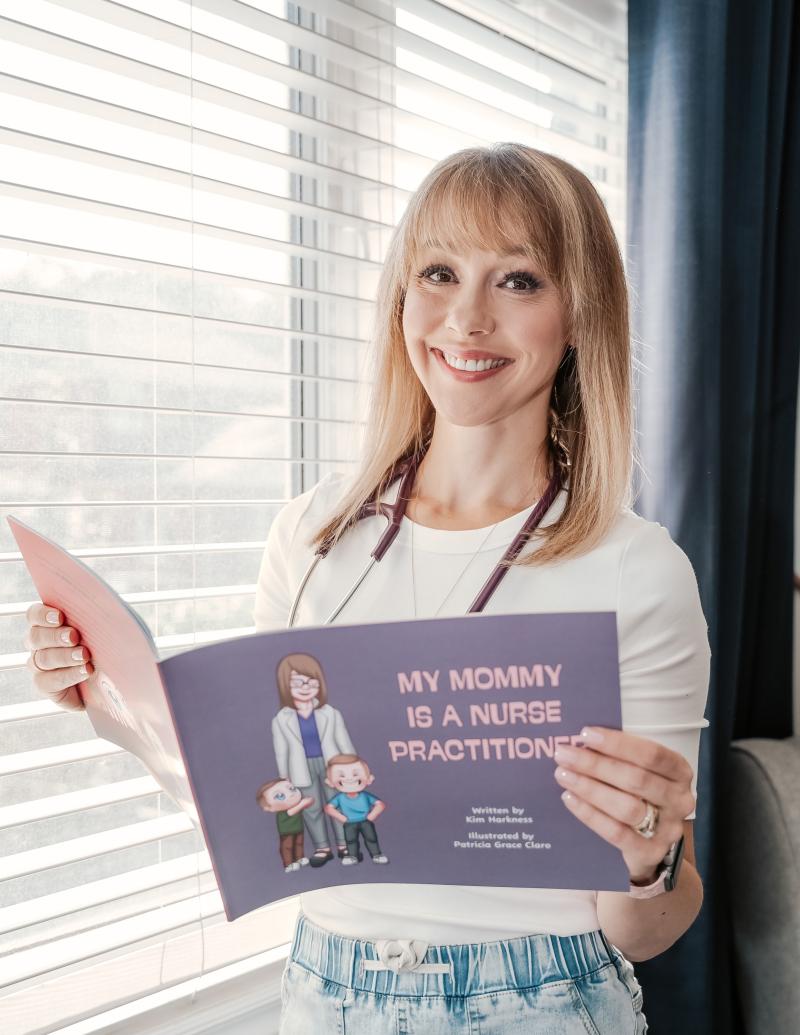 Kim standing by a window holding her book open and smiling