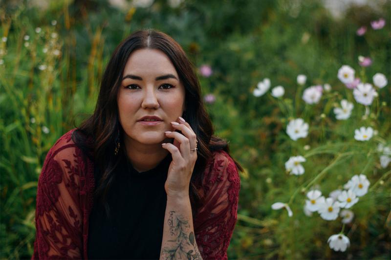 Karen McBride leans forward and looks serious in a meadow with wildflowers.