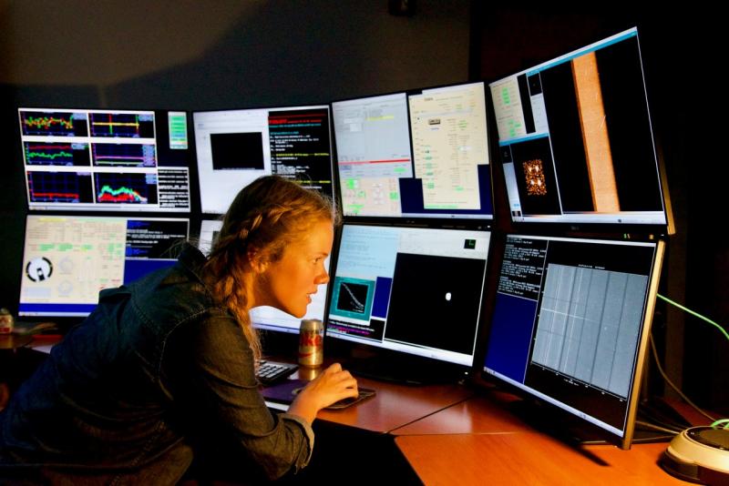 Katie Harris works in front of a bank of eight computer monitors, all displaying different information.