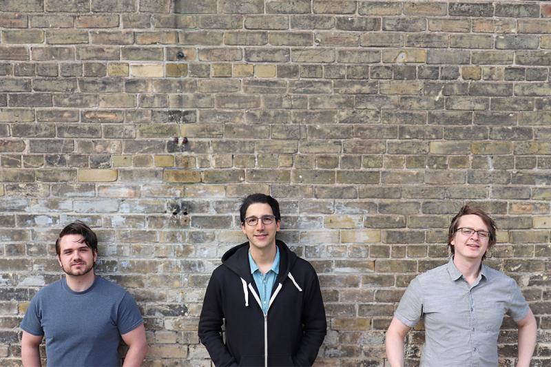Chris Leichthammer, Aidan Tinafar and Alex Klenov smile as they pose in front of a brick wall.