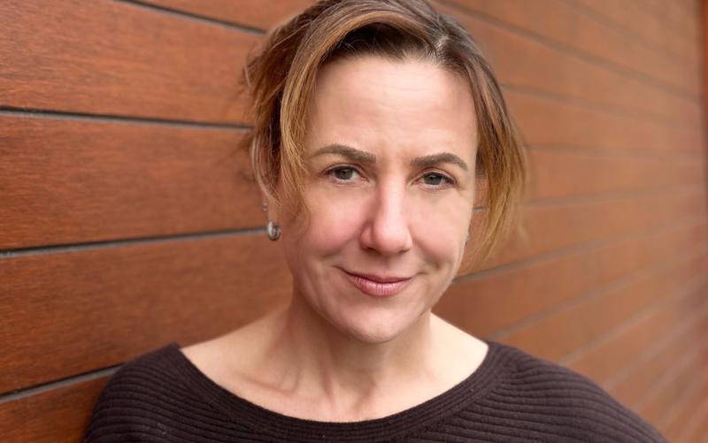 Lisa Hepner smiles, standing by a brick wall.