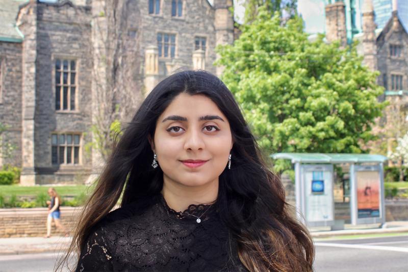 Sara Imran smiles quietly while standing on a sunny street.