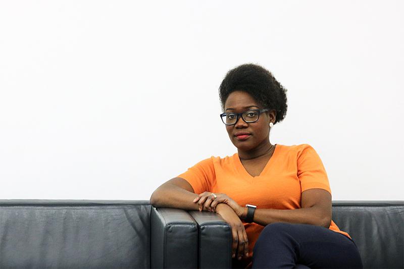 Onya Nnorom looks thoughtful as she leans on the arm of a sofa.