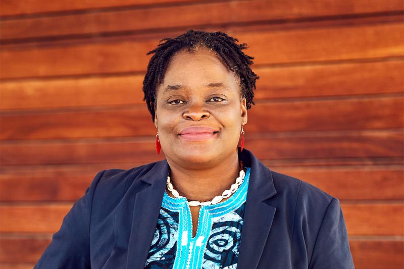 Roberta Timothy smiles, standing in front of some wood panelling.