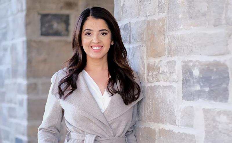 Rumeet Billan smiles as she stands outdoors by a stone wall.