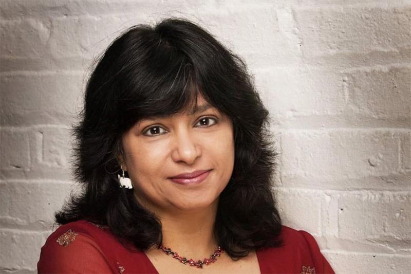 Anna Banerji looks thoughtful, standing by a painted brick wall.
