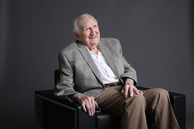 Lou Siminovitch sitting in an armchair and laughing.