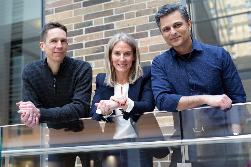 Tomi Poutanen, Mara Lederman and Muhammad Mamdani smile and lean on a balcony railing together.