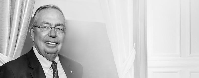 Portrait of Arthur Scace smiling, standing by a curtain indoors.