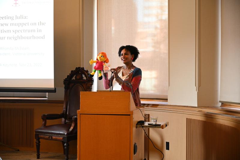 Rhonda McEwen stands at a podium with her puppet Julia