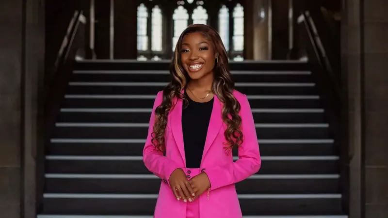 Portrait of Tobi wearing a neon pink suit and standing in front of an old wooden staircase