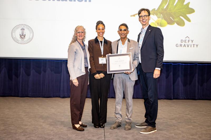Dr. Vivian Rambihar accepts his award on stage from three other people, Carl Mitchell's wife Margaret Shaw, daughter Nancy Mitchell and UTAA President Corwin Cambray.