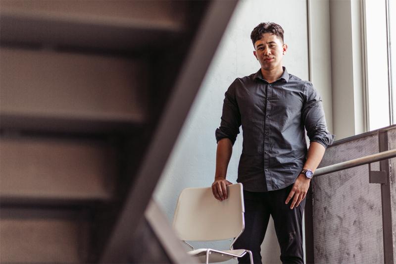 Christian Cordero looks serious as he stands near a bright window under a staircase.