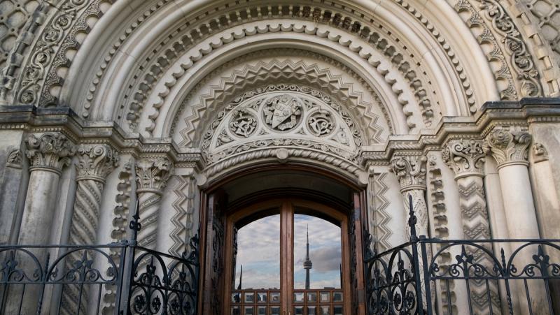The Toronto skyline with CN Tower is reflected in a door framed by an elaborately carved stone archway.