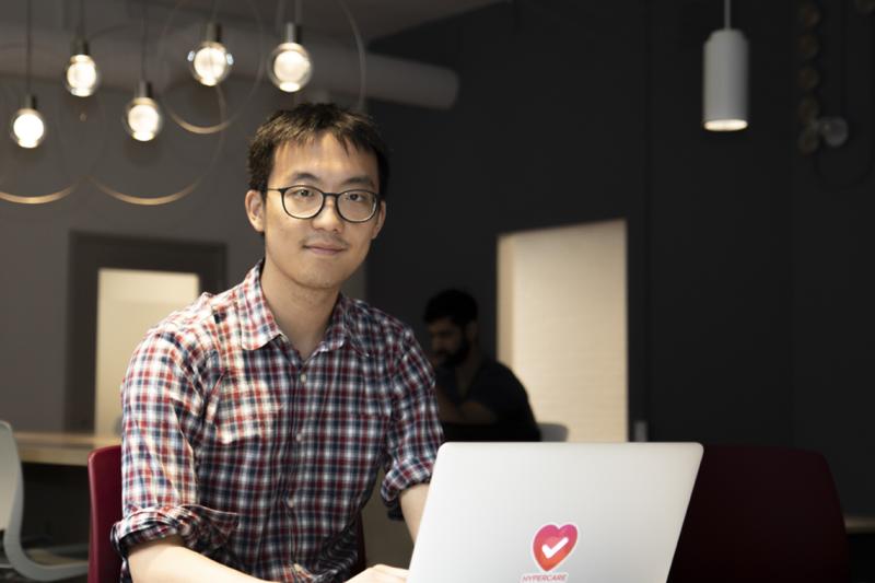 Albert Tai smiles as he looks up from a laptop with the Hypercare logo on its back.