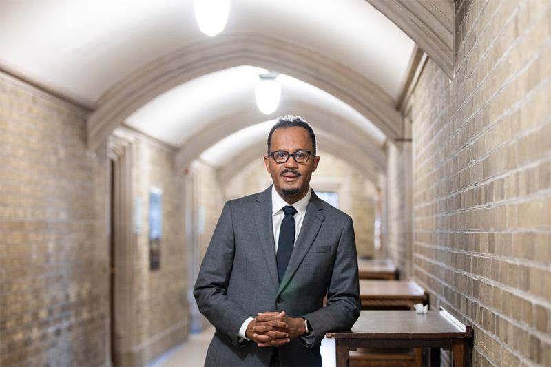 Dexter Voisin smiles as he stands in a vaulted hallway.