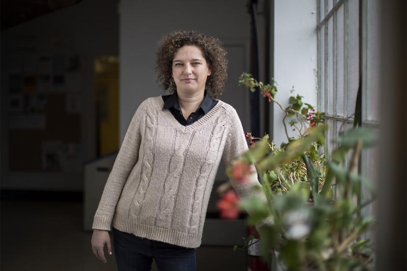 Shannon Simpson looks thoughtful as she stands by a window, the sill lined with potted plants.
