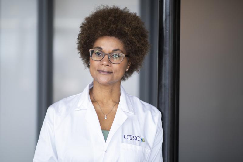 Maydianne Andrade looks serious, standing in a hallway wearing a lab coat with the U of T Scarborough logo.