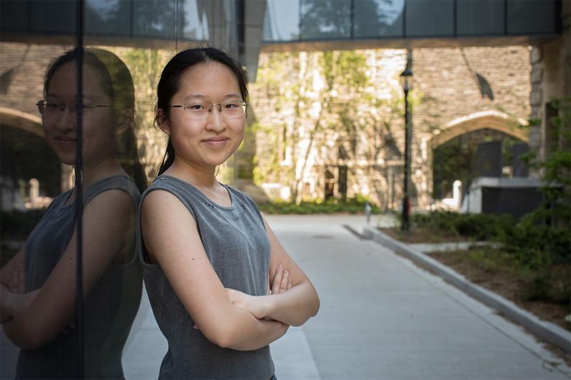 Maddy (Xiaoxiao) Zhang smiles as she leans on a reflecting wall in a sunny courtyard.