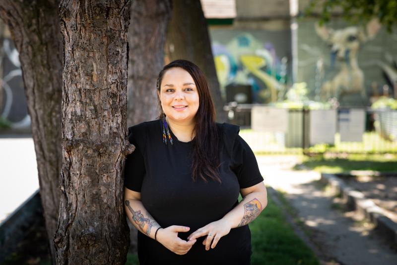Andrea Johns smiles as she leans on a tree outdoors.