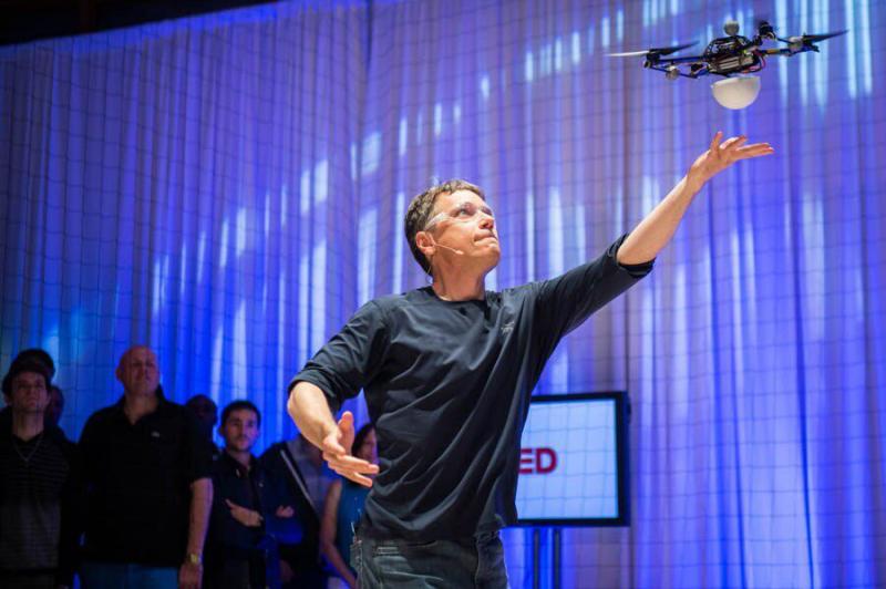 Raffaelo D’Andrea reaches up to a small drone hovering just above his hand.
