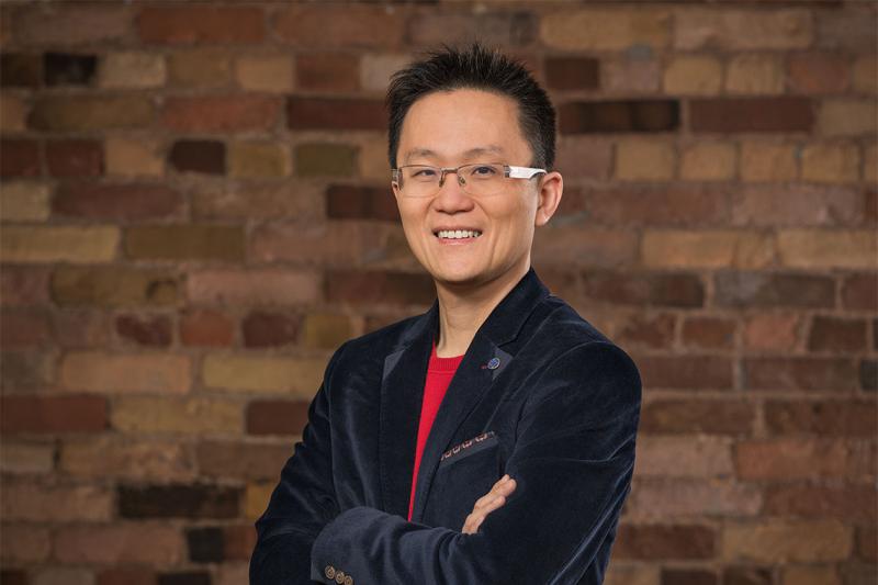 Allen Lau smiles as he stands with arms folded.