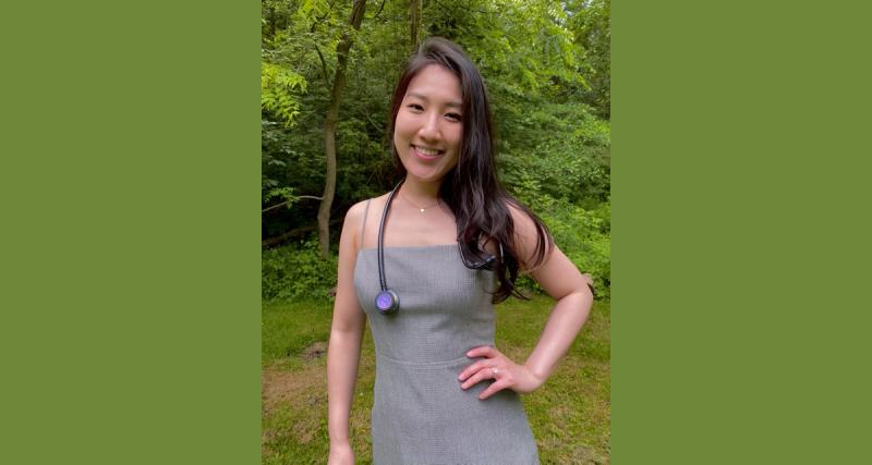 Yukei Ng smiles as she stands in a garden with one hand on her hip.