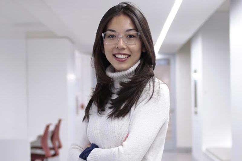 Kimberly Ren smiles with arms folded, standing in a bare indoor office room.