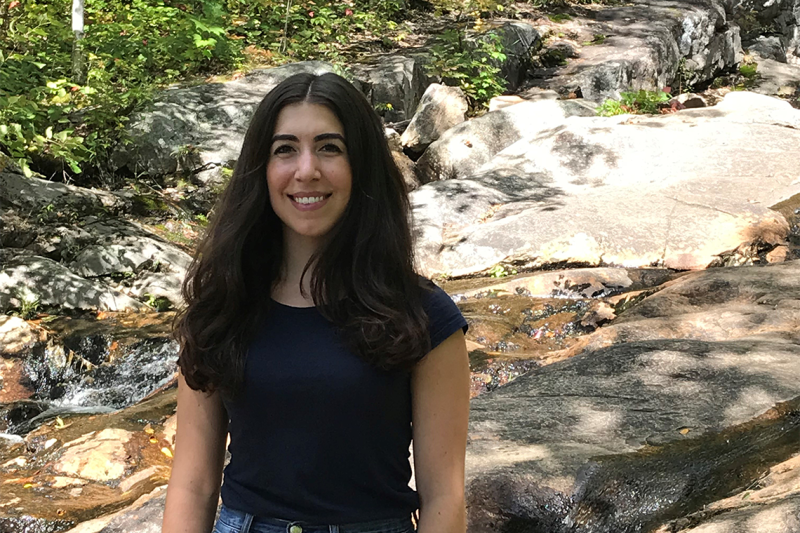 Anastasia Boutziouvis smiles, standing by a rocky stream outdoors.