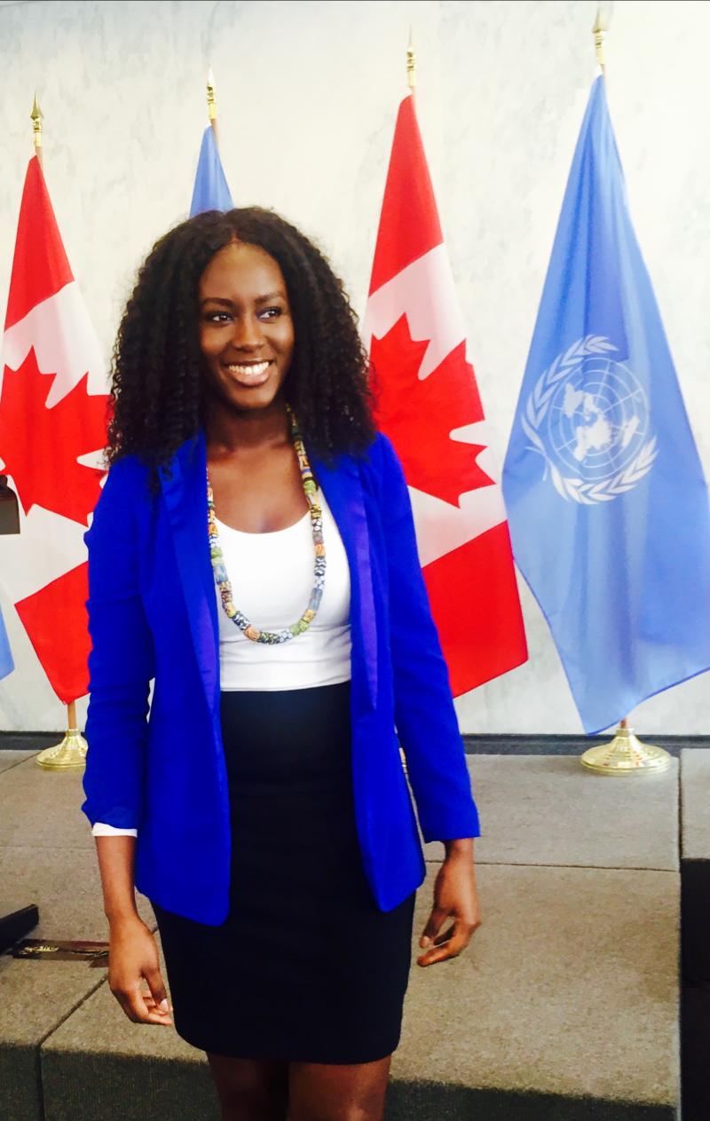 Binta Bajaha standing in front of two Canadian flags and two UN flags
