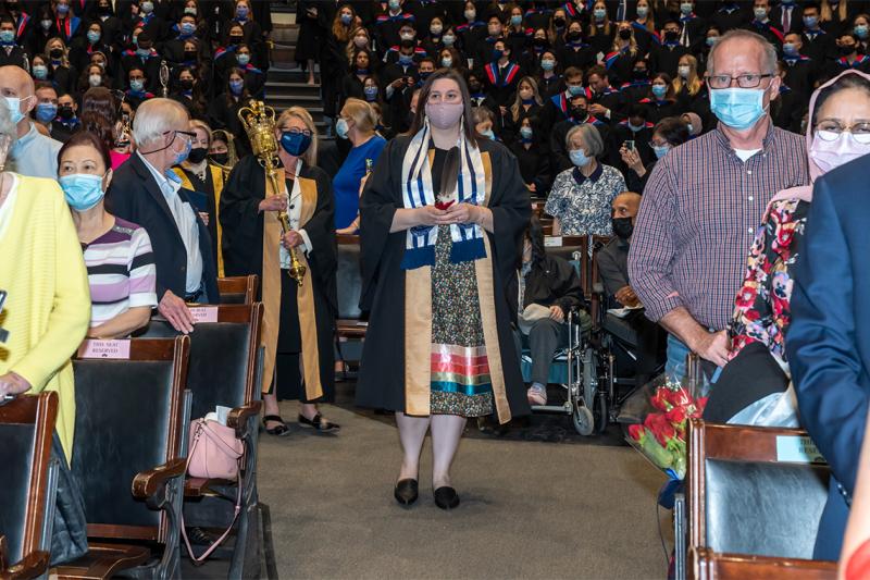 The audience in Convocation Hall stands as Lindsey Fechtig walks down an aisle holding an eagle feather.