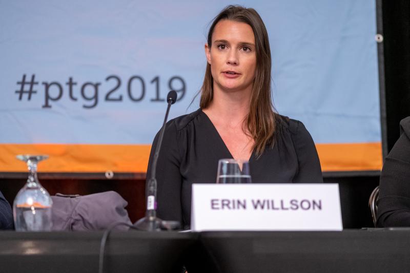 Erin Willson speaks as she sits at a conference table. On the screen behind is the hashtag #ptg2019.