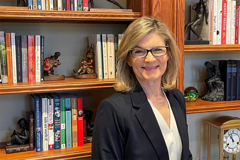 Gretchen Kerr smiles, standing in front of shelves full of books and whimsical carved bookends.
