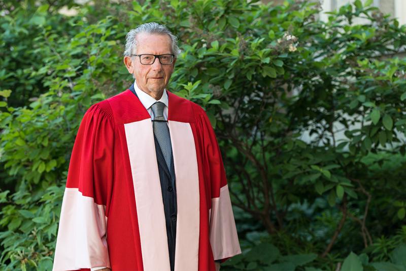 Ira Gluskin stands in a garden, wearing U of T academic robes.
