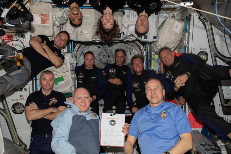 11 people pose together, floating in the air in a space station.
