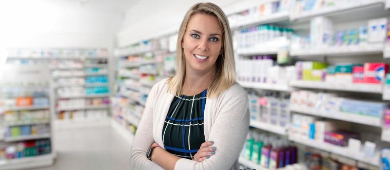 Kristen Watt smiles as she stands in front of pharmacy shelves.