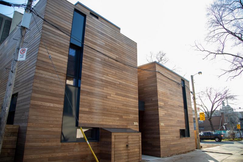 Polished wooden strips catch the sun as they line the walls of two buildings in a quiet alley.
