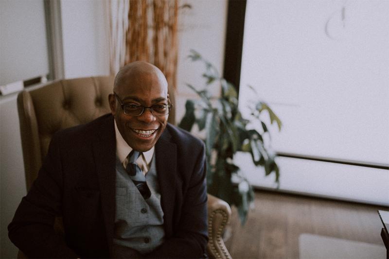 Lesra Martin laughs as he sits in a leather chair in an office.