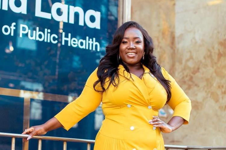 Maame De-Heer smiles happily, standing with hand on hip outside the Dalla Lana School of Public Health.