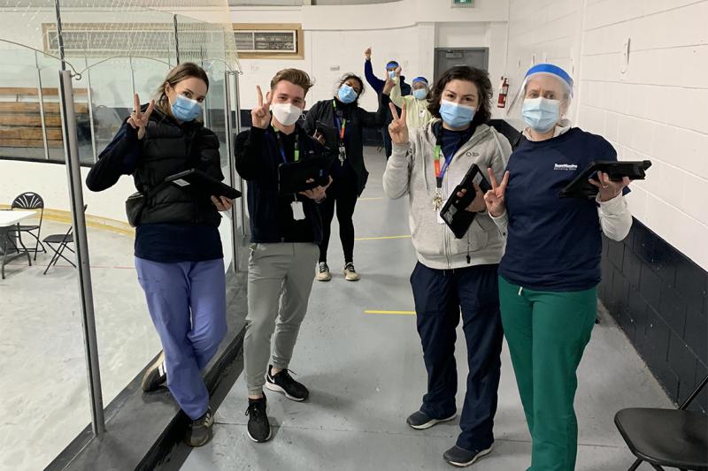 Susannah Merritt, Noah Schonewille, Upasana Saha, Cass Mackey and Erin Bearss flash victory signs at a vaccination clinic.