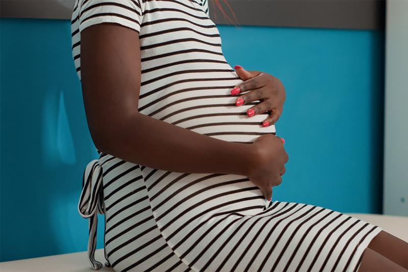 A pregnant black patient sits rubbing her belly