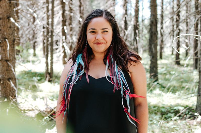 Samantha Martin-Bird smiles as she stands in a forest on a sunny day.