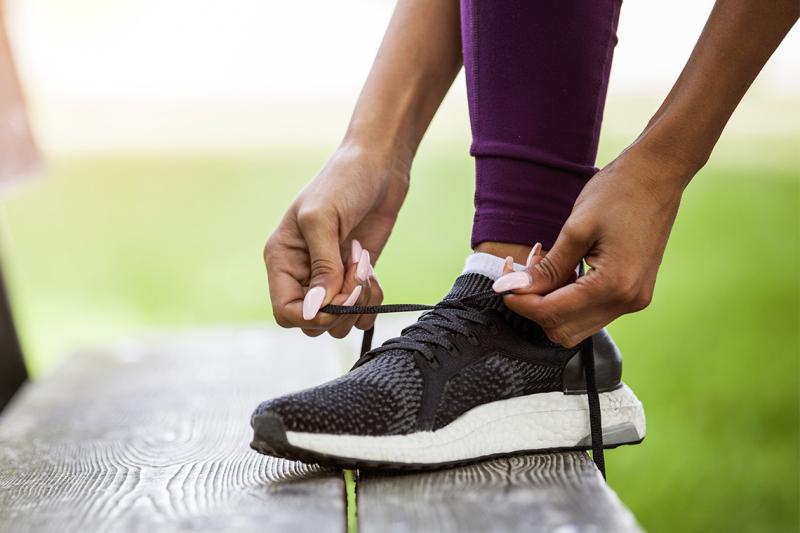Close up on a person's hands tying a running shoe, on a bench outdoors.