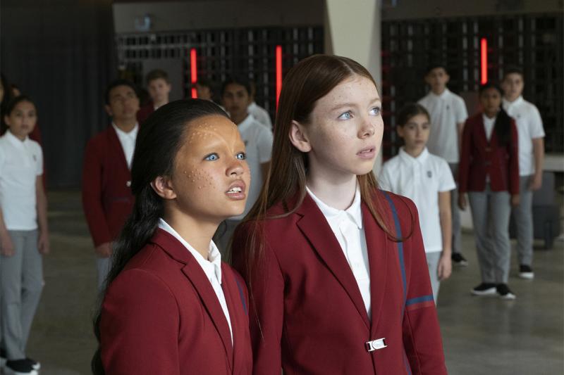 Two children wearing prosthetic makeup stand in front of several other kids wearing a school uniform.