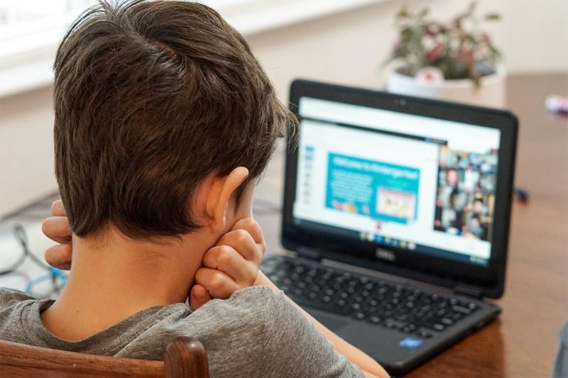 A young boy looks at a laptop screen with his head in his hands.