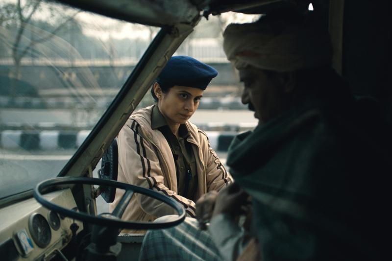 A woman in uniform looks doubtful as she peers through a bus window at a bus driver sitting in his driving seat.