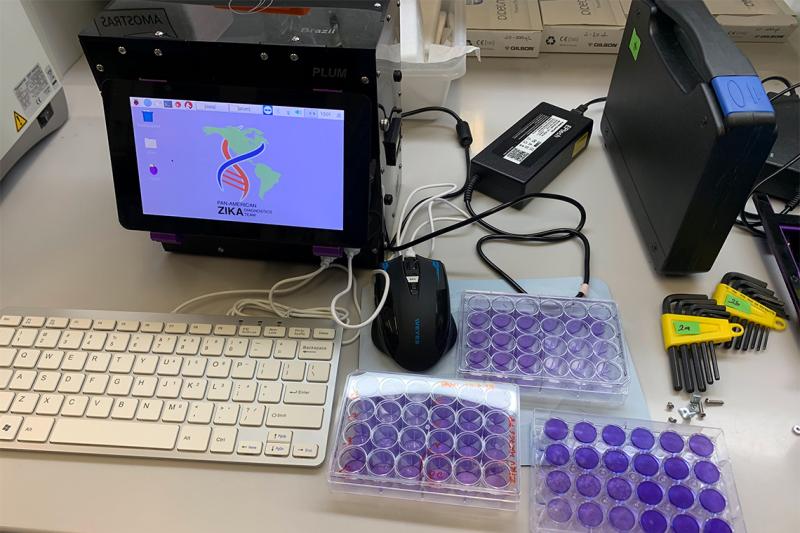 The elements of the portable rapid Zika virus test sit on a table: briefcase-sized machine, computer monitor, tray of vials.