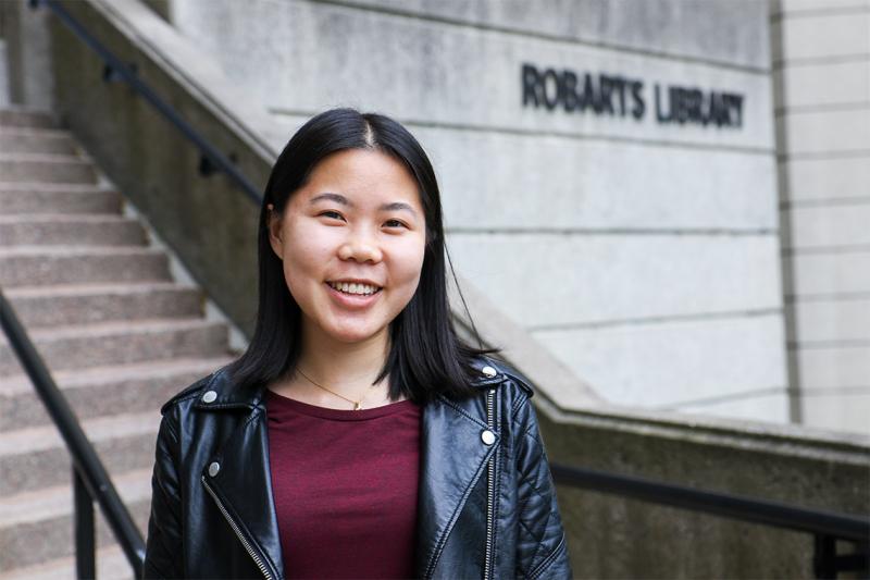 Danielle Lee smiles while standing in front of the steps to Robarts Library.